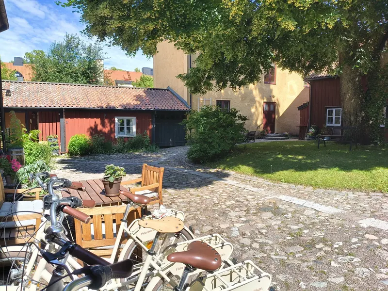 Kullerstensgården med trädgårdsmöbler, cyklar och gräsmatta mellan gula och röda hus